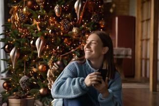 Woman smiling in front of Christmas tree holding phone.