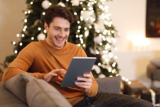 Man sitting by Christmas tree holding a tablet.