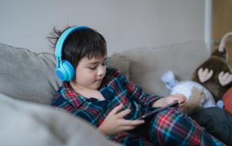 Young boy wearing headphones while playing on tablet.